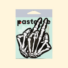 Load image into Gallery viewer, Pastease Middle Finger Skeleton Hand Pasties in black and white glow-in-the-dark design, featuring boney hand nipple covers for all breast shapes and sizes. Made in the USA by a small family business, these fun and flirty nipple covers are perfect for parties or bold looks.