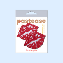 Load image into Gallery viewer, Kisses: Sparkly Red Kissing Puckered Lips Nipple Covers by Pastease. Two glitter red kissing lip shaped nipple covers shown in the pastease packaging on a pastel blue background.