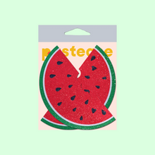 Load image into Gallery viewer, The Watermelon Slice with a Bite Breast Pasties by Pastease®. Two glittery velvet watermelon slices with some black heart shaped seeds with a bite mark out of it nipple covers shown in the pastease pastel packaging on a mint green background. Perfect for a festival, burlesque performance, drag shows, pride or parties.