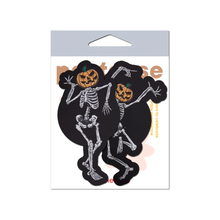 Load image into Gallery viewer, Dancing Skeletons Pasties with Pumpkin Heads Spooky Scary Skeletons nipple covers in their packet on a white background. One of the skeletons is dancing with one leg in the air and both arms up, while the other is dancing with arms bent and legs together. Both skeletons have orange spooky faced pumpkin heads.