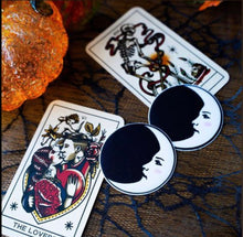Load image into Gallery viewer, Two Moon: Black and White Man in the Moon Nipple Pasties by Pastease shown next to two tarot cards and glass pumpkins on a black net table cover.