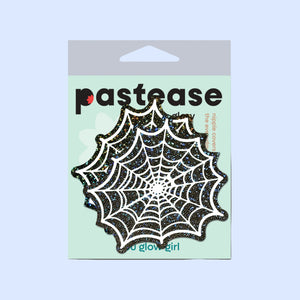 Packaging for Web: Glitter Black Glow in the Dark Spooky Spider Web Nipple Covers by Pastease®. Features a pair of glittery black and white spiderweb-shaped nipple covers on a mint green backing card with 'Pastease' branding. Designed for all breast shapes and sizes, handmade in the USA.