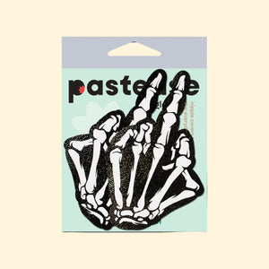 Pastease Middle Finger Skeleton Hand Pasties in black and white glow-in-the-dark design, featuring boney hand nipple covers for all breast shapes and sizes. Made in the USA by a small family business, these fun and flirty nipple covers are perfect for parties or bold looks.