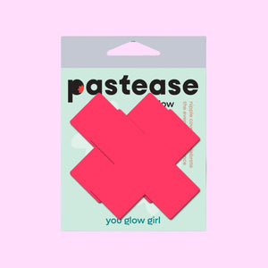 Plus X Glow-in-the-Dark Neon Pink Cross Pasties Nipple Covers by Pastease® in original packaging. The packaging is mint green with bold black branding and a “You Glow Girl” tagline. The vibrant pink pasties are front and centre, shaped like thick cross symbols.