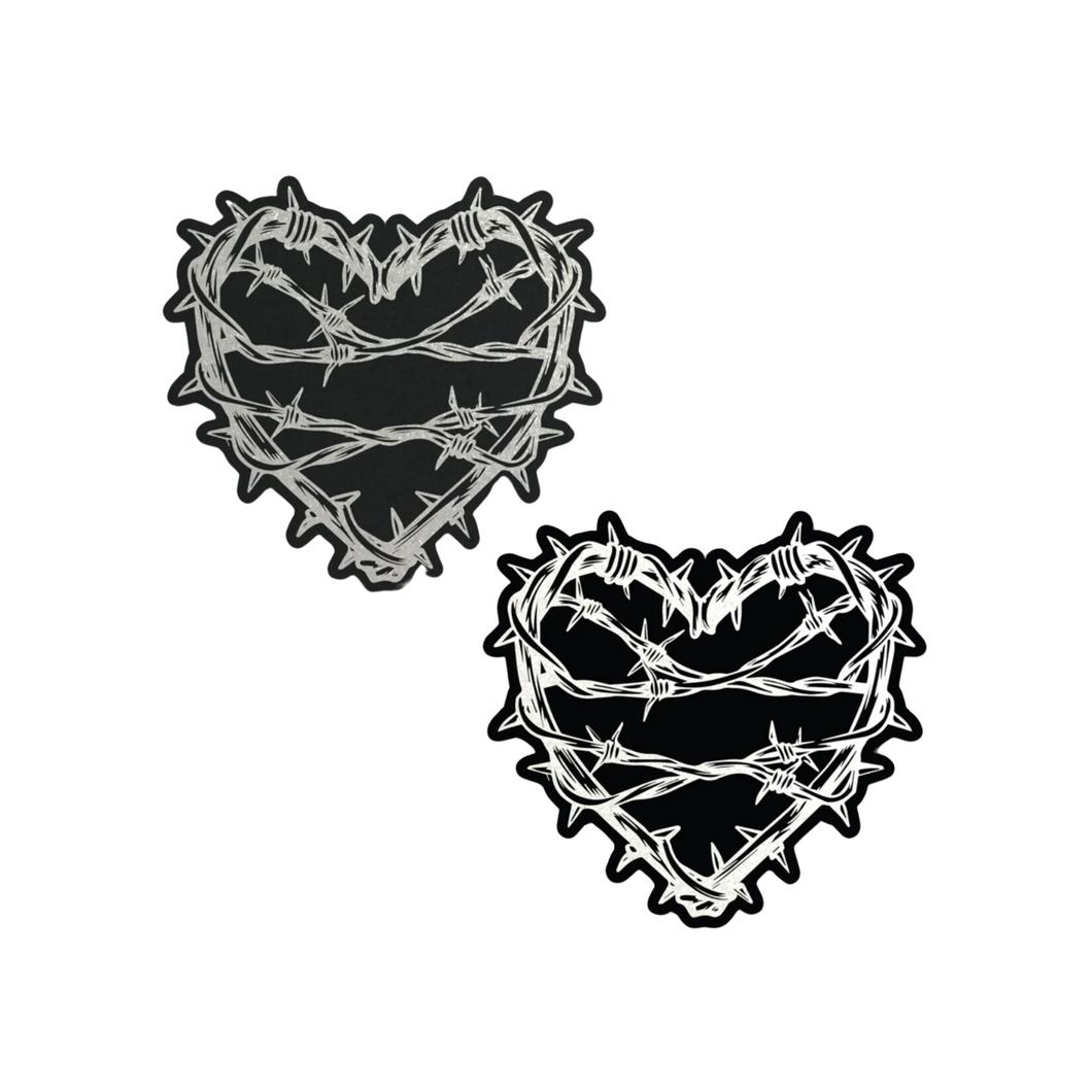 The Barbed Wire Heart Pasties Reflective Nipple Covers by Pastease®. Two black hearts with silver reflective barbed wire patterned shaped nipple covers shown on a white background. Perfect for festivals, pride, burlesque, raves, only fans content or parties.