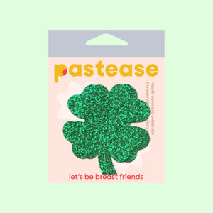 The Four Leaf Clover: Glittering Green Shamrocks Nipple Pasties by Pastease® in the pastease pastel cellophane packaging on a pastel green background. Two green glitter four leaf clover nipple covers. Perfect for a festival, burlesque performance, drag shows, pride or parties.