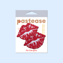 Load image into Gallery viewer, Kisses: Sparkly Red Kissing Puckered Lips Nipple Covers by Pastease. Two glitter red kissing lip shaped nipple covers shown in the pastease packaging on a pastel blue background.
