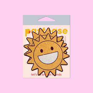 The Happy Sun Pasties Sparkling Smiling Sunshine Nipple Covers by Pastease®. Two smiling glitter velvet cartoon sunshine nipple covers shown in the pastease pastel packaging on a pastel pink background. Perfect for a festival, burlesque performance, pride or parties.