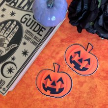 Load image into Gallery viewer, Pumpkin: Spooky Halloween Jack O&#39; Lantern Nipple Pasties by Pastease. Two orange smiling carved pumpkins nipple covers on an orange fluffy background with various witchy items such as palmistry guides and black flowers surrounding them.
