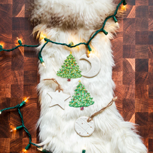 Load image into Gallery viewer, Christmas Tree Nipple Pasties by Pastease®. Two green glittery Christmas tree shaped nipple covers, shown on white fur background with star and moon Christmas decorations and fairylights. Perfect for a festival, burlesque performance, pride, Christmas or parties
