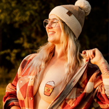 Load image into Gallery viewer, Model in plaid orange shirt and bobble hat smiling in the golden sun on an Autumn&#39;s day with shirt pulled to the side to reveal the Pastease pasties Pumpkin Spices nipple cover nipple cover on model&#39;s breast.
