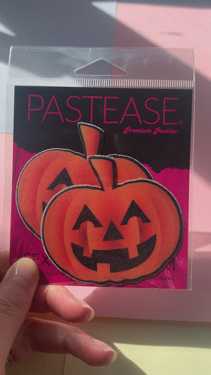 Pumpkin: Spooky Halloween Jack O' Lantern Nipple Pasties by Pastease in pink and black cellophane packaging being shown in the sunlight.