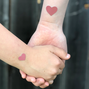 Pastease Confetti: Liquid Black Baby Heart & Star Body Pasties by Pastease®. Two mini blush pink hearts shown on the wrists of two people holding hands.