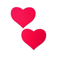 The Love: Neon Red (Blacklight Reactive) Heart Nipple Pasties by Pastease. Two neon red heart nipple covers on a white background. Perfect for a festival, pride, burlesque performance, only fans content or a party.
